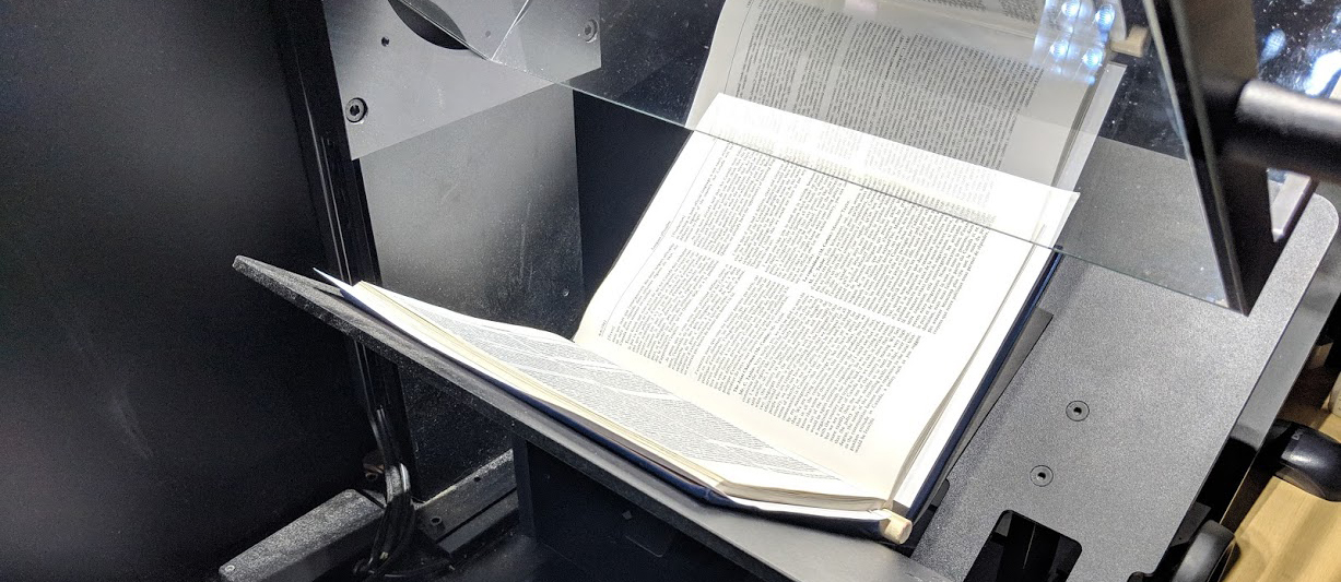 An open book sits inside a digital scanner.
